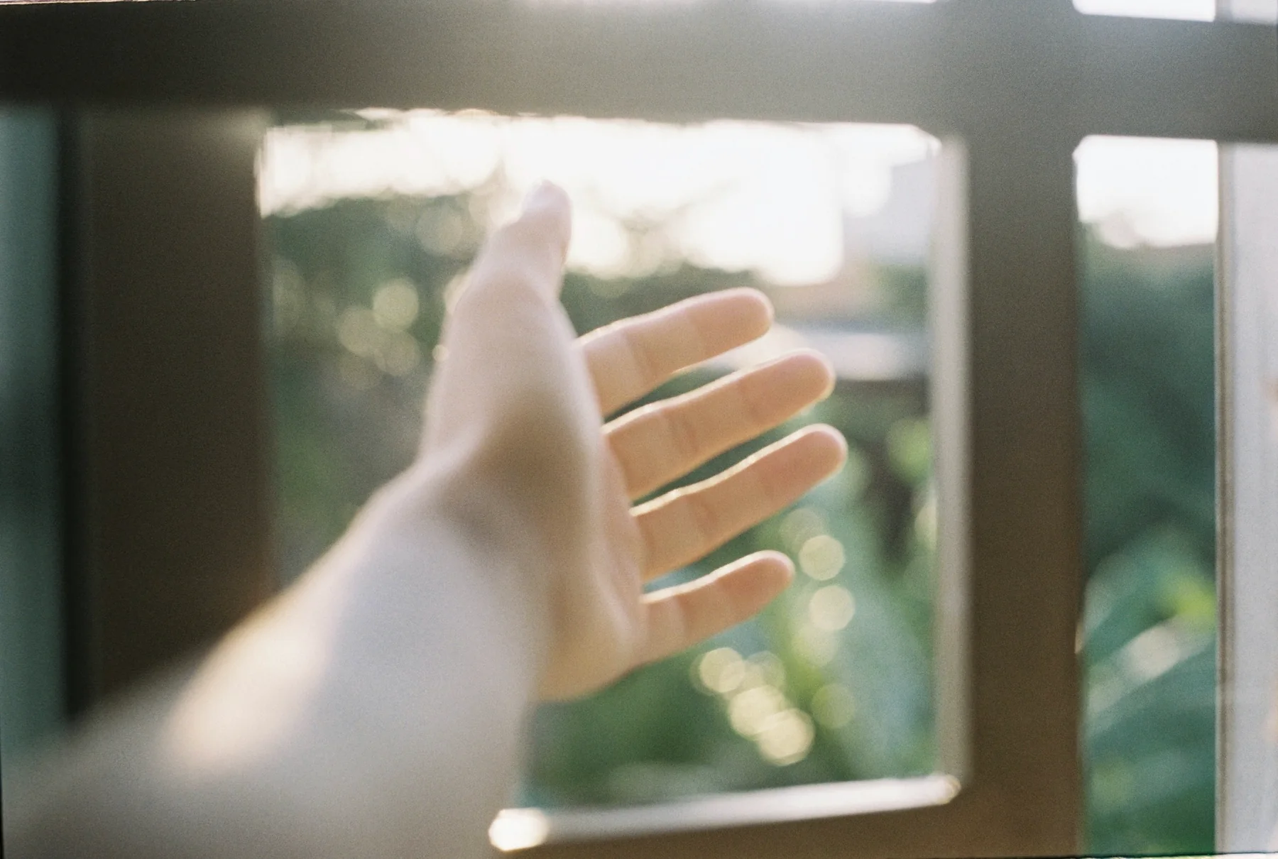 A hand reaching toward changing light through a window
