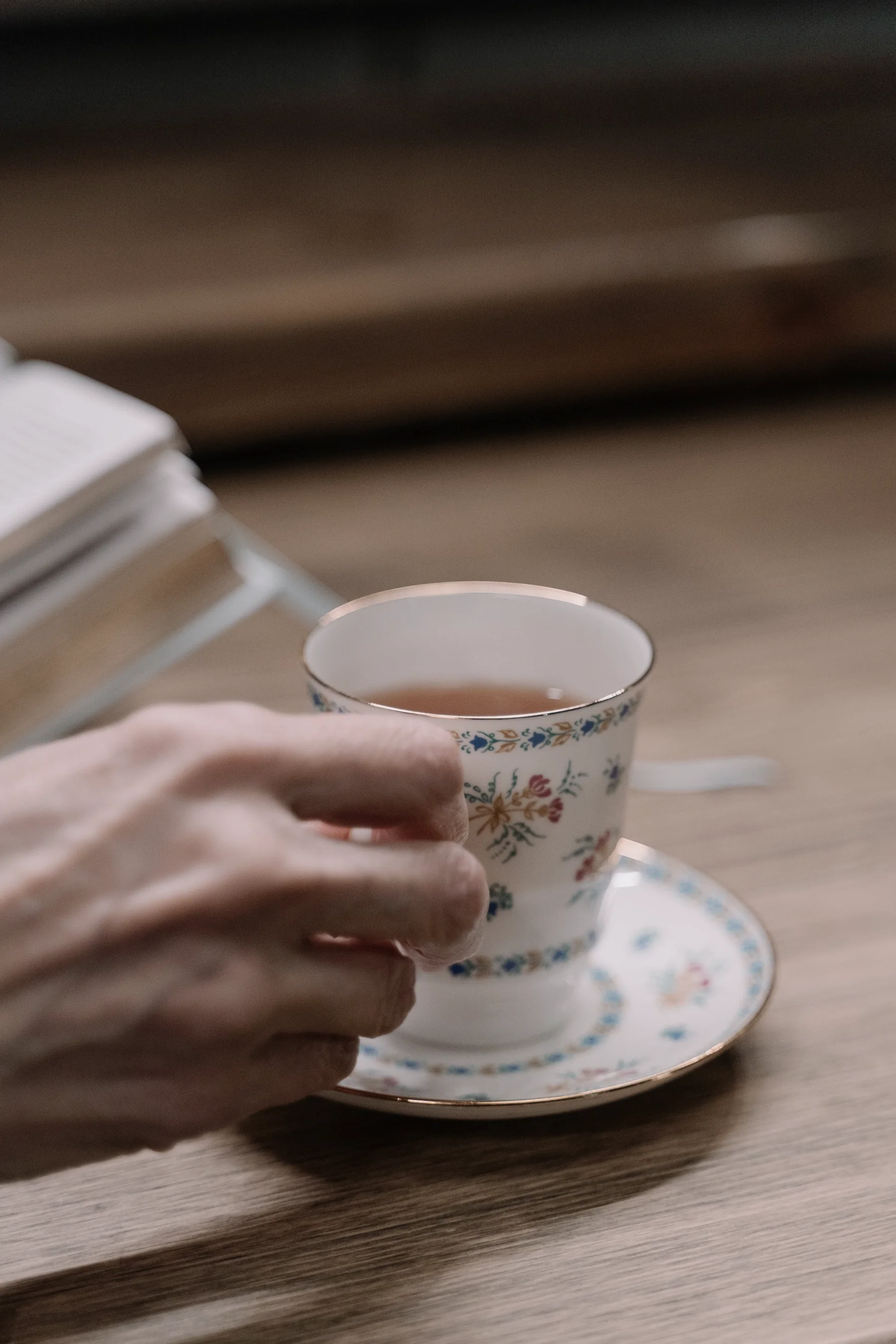 A hand resting beside a cup of tea and a book